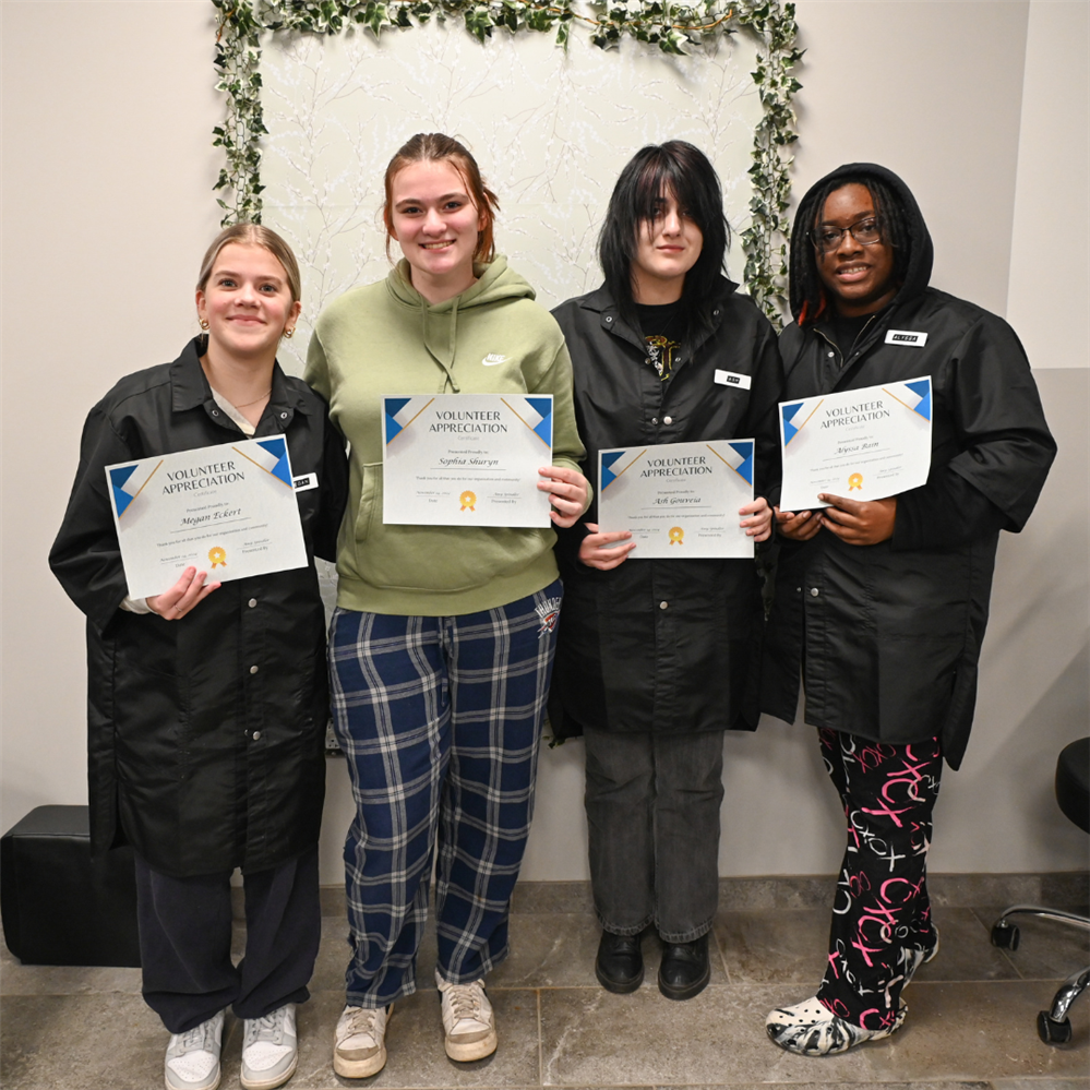  Four Cosmetology students smile with their certificates of appreciation.